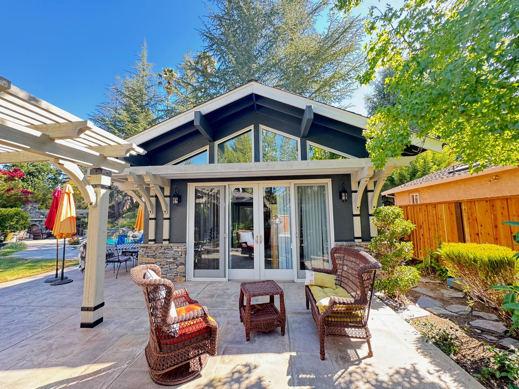Finished backyard living space with repainted craftsman-style home, stone accents, and pergola